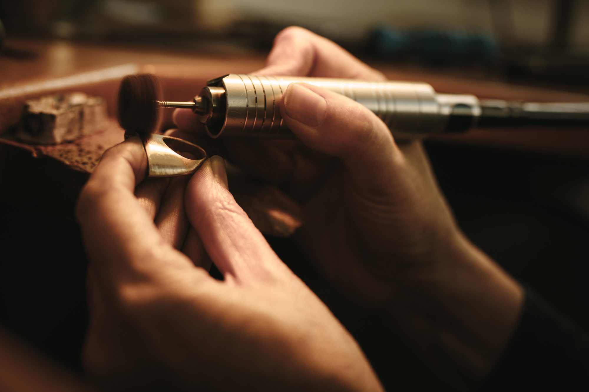Hands of woman jeweler polishing a ring surface with grinding machine. Goldsmith making a piece of jewelry at her workbench.